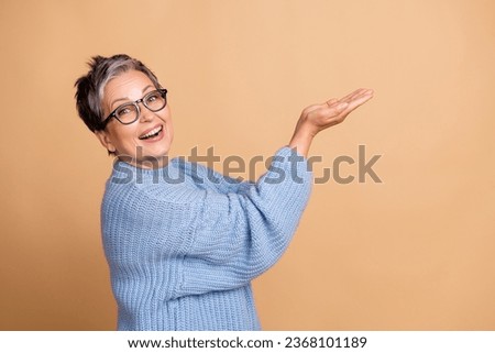 Photo portrait of attractive senior woman palms hold empty space dressed stylish blue knitted clothes isolated on beige color background