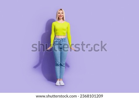 Full size photo of lovely friendly girl wear stylish yellow shirt denim pants standing like doll isolated on violet color background