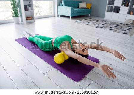 Photo of dreamy smiling young girl dressed sportive suit lying mfr roll stretching back indoors house home