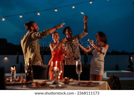 Group of friends wearing formal wear while having a dinner party and drinking at night by the swimming pool vawing sprinkles Royalty-Free Stock Photo #2368111173