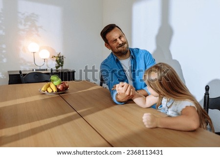 Father pretending to be losing at arm wrestling with his toddler daughter while she is having fun and smiling