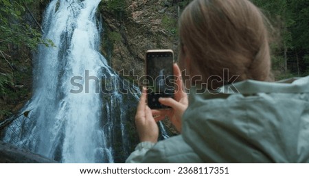 Woman takes pictures on the phone while traveling in Austria. Girl tourist films Golling waterfall in mountain forest.