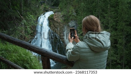Girl tourist films Golling waterfall in mountain forest in Austria on her phone.