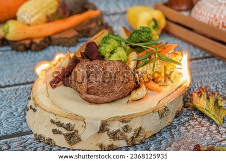 Delicious filet mignon steak with grilled vegetables.Steak filet minion, bbq steak  beef. On a wooden stump and a wooden background. Parchment paper is burning