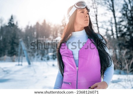 Portrait of a beautiful young female skier. Attractive sportswoman wearing pink ski suit and goggles standing outdoors and being thoughtful.
