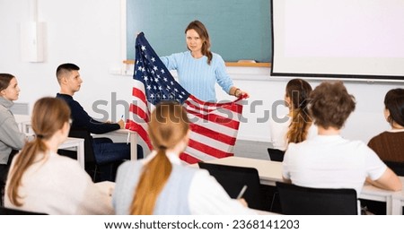 Geography lesson in school class - teacher talks about United States of America, holding a flag in his hands