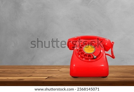 Red vintage desk phone on wooden table, cement background.