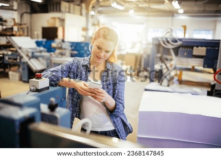 Young Caucasian woman using a smartphone while working in a printing press office