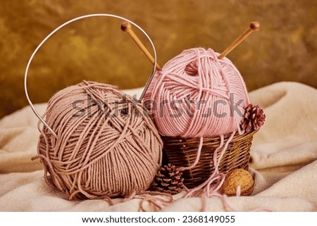 two skeins of pink and beige yarn with wooden and metal knitting needles in a basket with pine cones and nuts on natural linen fabric, winter cozy atmosphere Royalty-Free Stock Photo #2368149055