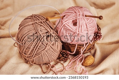 two skeins of pink and beige yarn with wooden and metal knitting needles in a basket with pine cones and nuts on natural linen fabric, cozy atmosphere Royalty-Free Stock Photo #2368150193