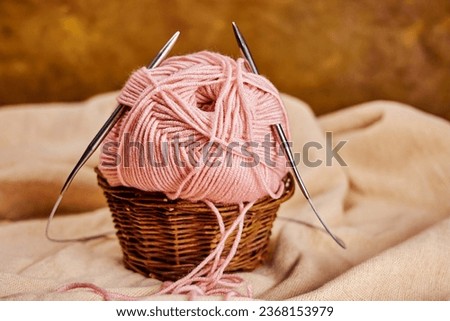 a skein of pink yarn with metal knitting needles in a basket on natural linen fabric, a cozy homely atmosphere Royalty-Free Stock Photo #2368153979