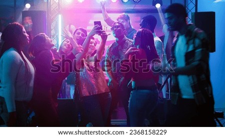 Friends taking pictures at disco party and having fun together on night out, dance event. Group of persons taking photos on phone, making fun memories at social celebration. Handheld shot.