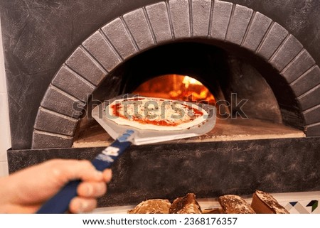 The chef prepares pizza. Raw pizza ready to bake. Cook in a apron in the kitchen. with a shovel in his hands. boxes for food delivery on background.