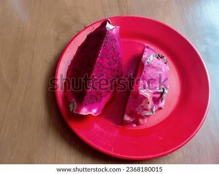 Sliced dragon fruit on a red plate, dragon fruit slices, dragon fruit is cut into 2 parts, the color is red, full of black seeds, the taste is sweet and fresh, at red plate, buah naga warna merah sega