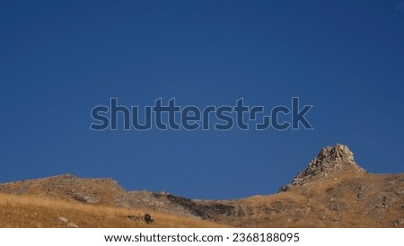 Low line of mountain horizon with blue sky. Creative. Beautiful natural background with rocky mountains and blue sky. Rocky mountains with dry grass on background of clear blue sky