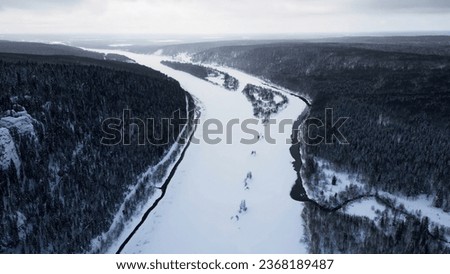 Aerial view of a bending snow covered river and forested valley. Clip. Frozen curving river flowing among dense forest.