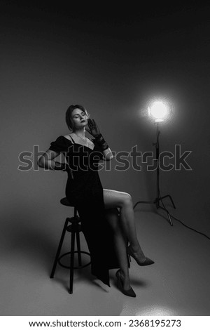 A woman model in a black dress poses in a photo studio in the spotlight. Monochrome shot.