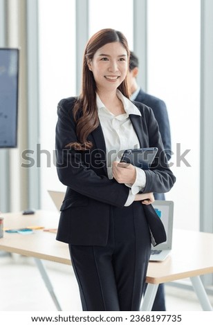 Portrait shot of Asian professional successful female businesswoman manager entrepreneur in formal suit standing smiling looking at camera holding touchscreen tablet computer in company meeting room.