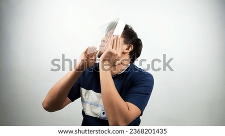 Portrait of Asian Man in blue and white shirt holding transparent box and trying to see the other side from inside.isolated white background