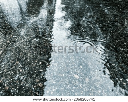 flooded pavement after heavy rain. water puddle with raindrops and reflection of sky.