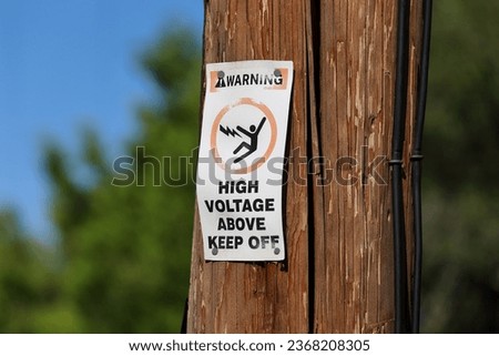 A Warning, High Voltage Above Keep Off sign on a wooden pole.
