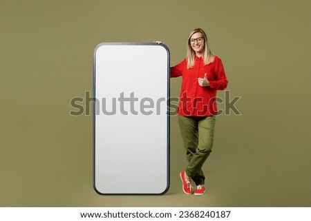 Full body smiling fun happy young woman she wears red shirt casual clothes glasses big huge blank screen mobile cell phone smartphone with area show thumb up isolated on plain pastel green background