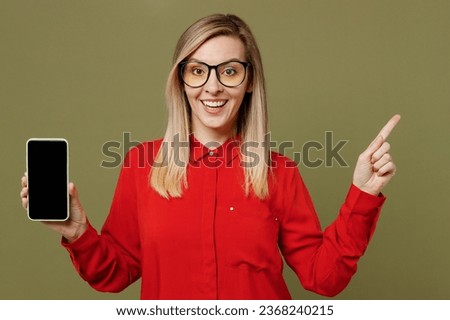 Young surprised woman she wearing red shirt casual clothes glasses hold in hand use mobile cell phone with blank screen workspace area pont index finger aside isolated on plain pastel green background
