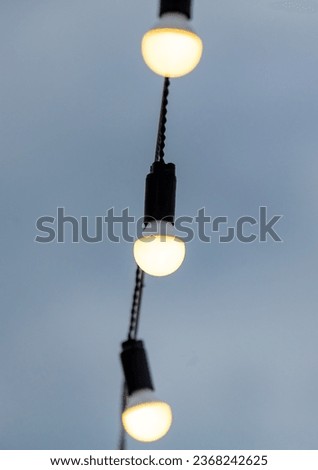 Festive light bulbs shine against the background of the sky with clouds.