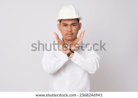 Young Asian engineer employee strict man in a protective helmet hardhat looking at camera while making stop gestures cross hands isolated on white background