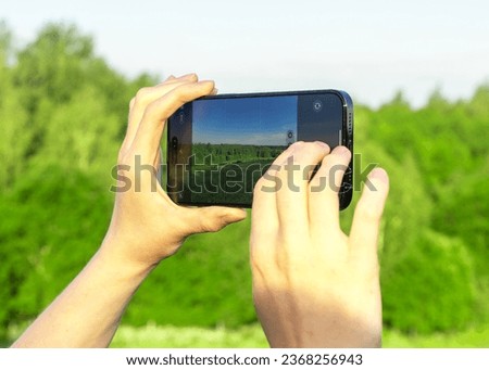 Hands holding mobile phone, taking photo of nature