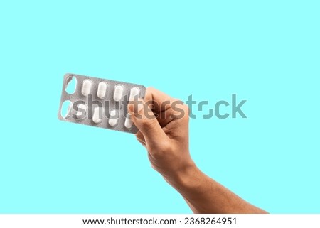 Hand holding blister pills on isolated cyan background Royalty-Free Stock Photo #2368264951