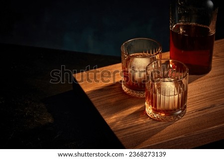 Top view of two glasses of whiskey, rum, brandy or bourbon with ice cube and bottle standing on wooden table over dark background. Concept of alcohol, strong spirits, drinks, liquid, restaurant, pub. Royalty-Free Stock Photo #2368273139