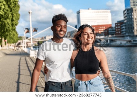 A colorful, urban evening by the riverside with two attractive, diverse models in casual attire, radiating joy. Royalty-Free Stock Photo #2368277745