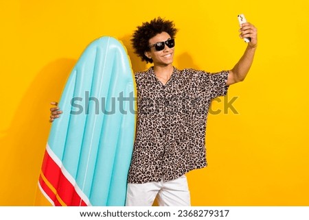 Portrait of cool person wear leopard shirt in sunglass hold surfboard make selfie on smartphone isolated on yellow color background