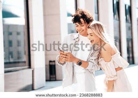 Young smiling beautiful woman and her handsome boyfriend in casual summer clothes. Happy cheerful family. Female having fun. Couple posing in street. Hold smartphone, use phone apps, look at screen