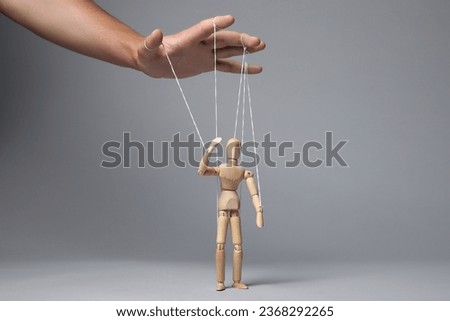 Man pulling strings of puppet on gray background, closeup Royalty-Free Stock Photo #2368292265