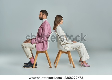 modern couple in business attire sitting back to back in armchairs on grey, minimalistic c fashion Royalty-Free Stock Photo #2368297673