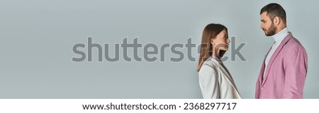 side view of young couple in stylish blazers looking at each other on grey, business fashion, banner Royalty-Free Stock Photo #2368297717
