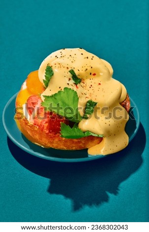 Poached eggs with liquid yolk, tomato, bacon and cheese sauce on toasted bun on plate on cyan background. Concept of breakfast, food, taste, creativity. Pop art photography. Poster. Copy space for ad