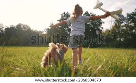 the girl runs with the plane and the dog. happy family kid dream concept. girl daughter running across a field of green grass in the park playing with a toy airplane and a pet lifestyle dog