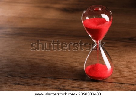Hourglass with red flowing sand on wooden table. Space for text