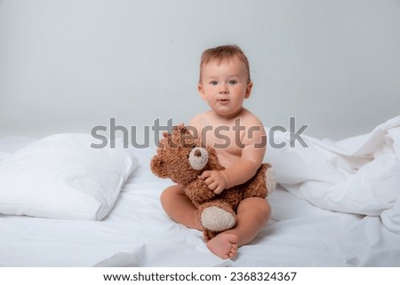 a little baby boy in the bedroom on the bed in a diaper playing with a teddy bear on a white background.