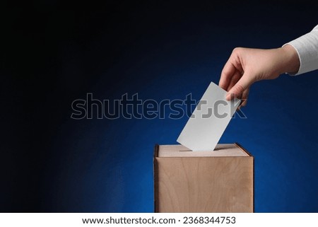 Woman putting her vote into ballot box on dark blue background, closeup. Space for text Royalty-Free Stock Photo #2368344753