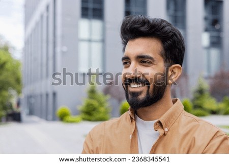Young dreamy man close-up smiling and looking to the side, portrait of a student businessman in the air outside an office building, in casual clothes. Royalty-Free Stock Photo #2368345541