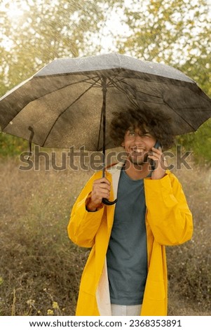 Arab man in a yellow raincoat under an umbrella from the rain talking on a mobile phone and smiling. Copy space