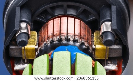 Closeup of electric DC motor rotor with copper winding fixed by blue epoxy in black plastic housing. Commutator with carbon brush contacts pressed by steel cylindric coil springs inside engine detail. Royalty-Free Stock Photo #2368361135