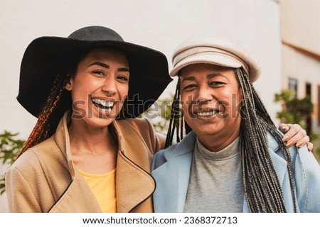 Happy african mother and daughter smiling in front of camera during winter time with city in background - Family and love concept