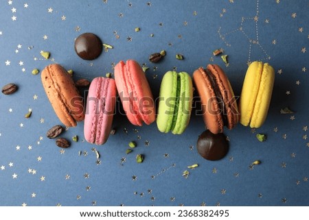 Tasty colorful macarons with chocolate, coffee, lemon, berries, and pistachio flavors on a pastel dark blue and gold stars background