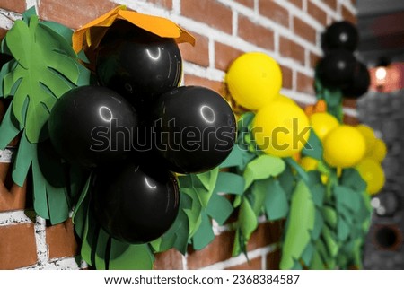 Bright objects, decorations on a brick wall, indoors, interior in the style of a Hawaiian party, tropics, jungle and black air helium balloons.