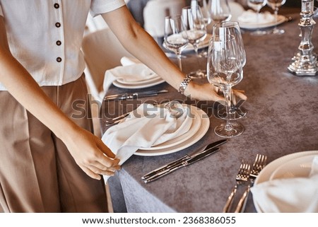 cropped view of event coordinator arranging festive setting on table with floral decor in event hall Royalty-Free Stock Photo #2368386055